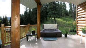 Una terraza de madera con jacuzzi, asientos y vistas a un cerro cubierto de bosque.