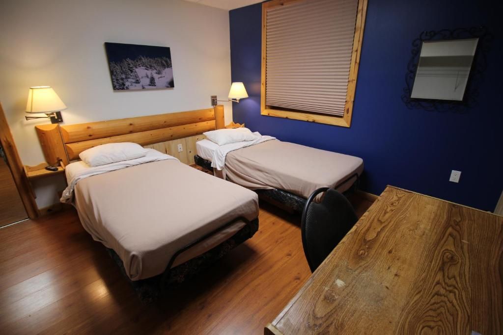 A room with two beds, a wooden table, and a window with blinds.