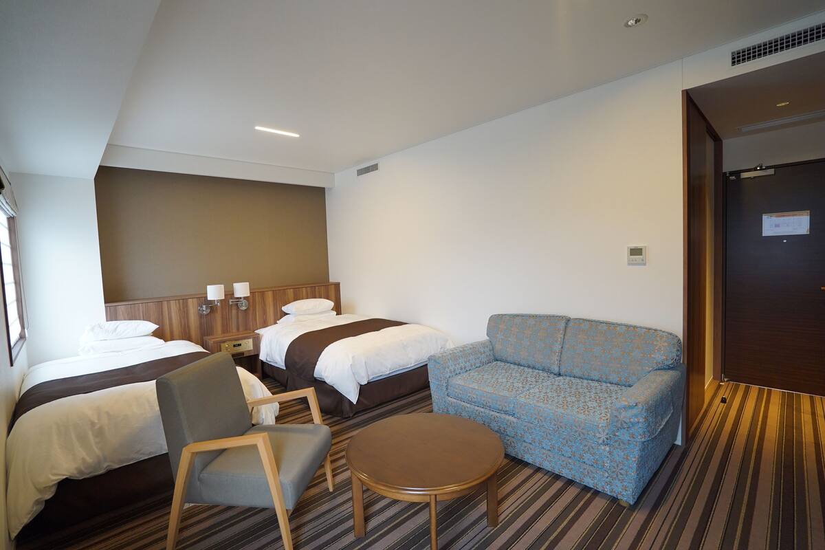 Een hotelkamer met twee bedden, een bank, een stoel en een kleine tafel.