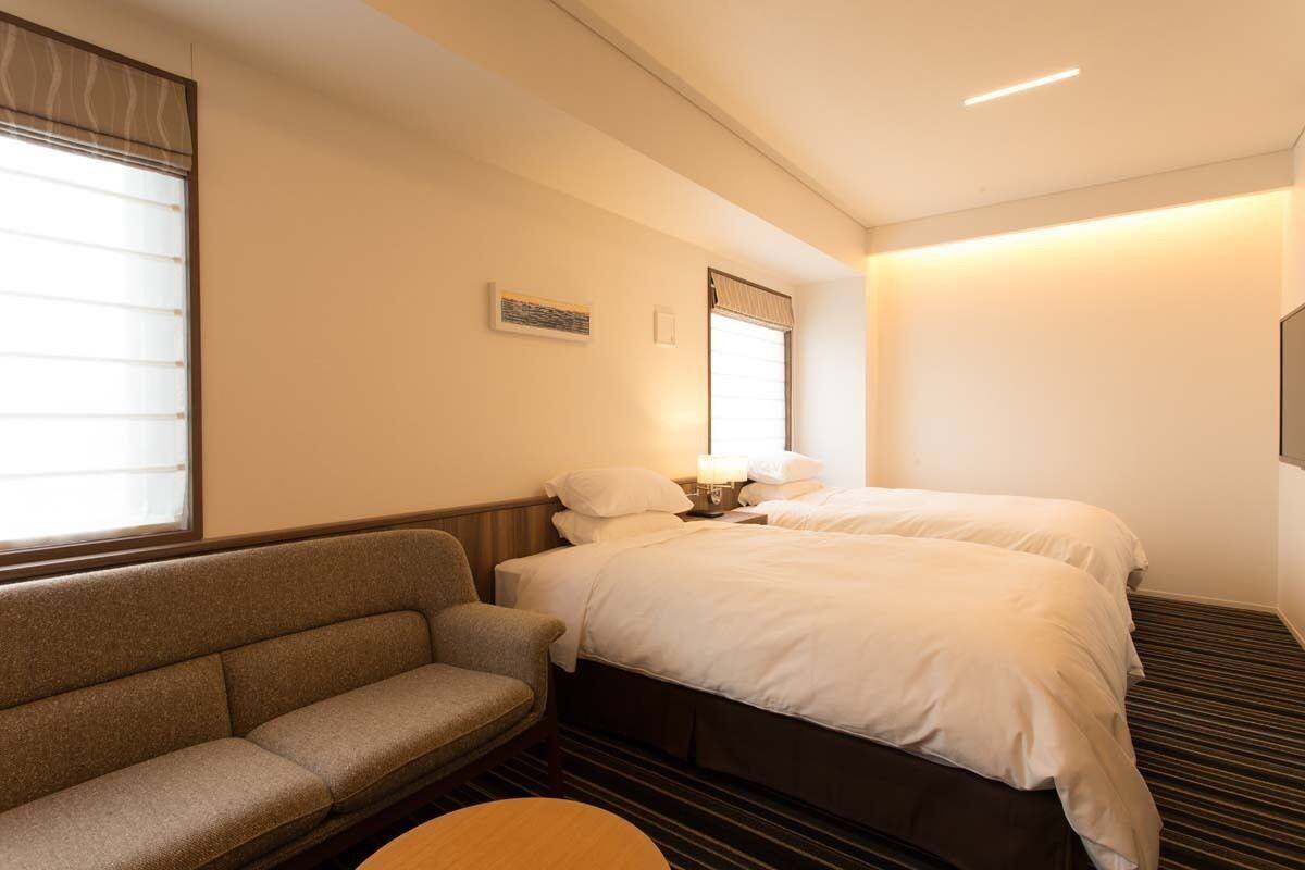 Een hotelkamer met een bed, een slaapbank, een kleine tafel en een raam met zonwering.
