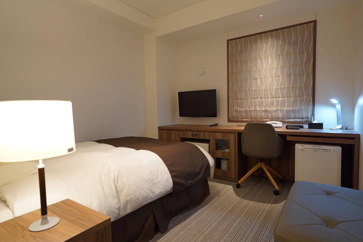 Een hotelkamer met twee bedden, een bureau met een computer, een stoel, een lamp en een kleine koelkast.