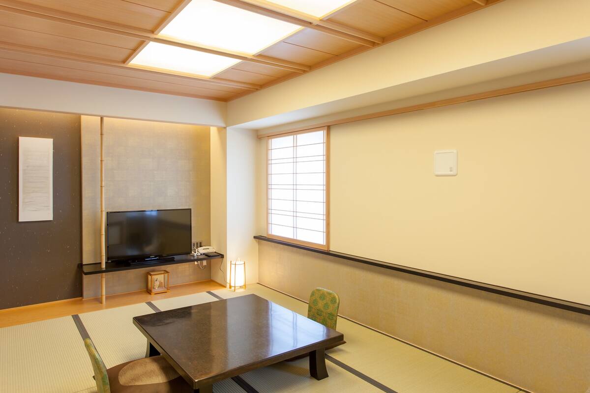 Een traditionele Japanse kamer met tatami vloerbedekking, een lage tafel, een televisie en een groot raam.