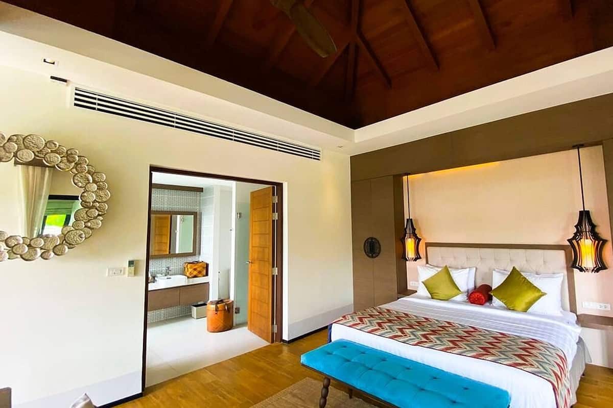 A bedroom with a large bed, a headboard with lights, a mirror, and a bathroom visible through an open door.