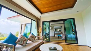 A modern living room with a wooden ceiling, large sliding glass doors leading to a balcony, and a view of the outdoors. - Silla Villa Private Pool & Sea View (Karon)
