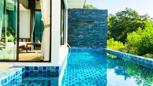 A modern pool with blue tiles, a glass door leading to a room with a bed and curtains, and a stone wall. - Silla Villa Private Pool & Sea View (Karon)