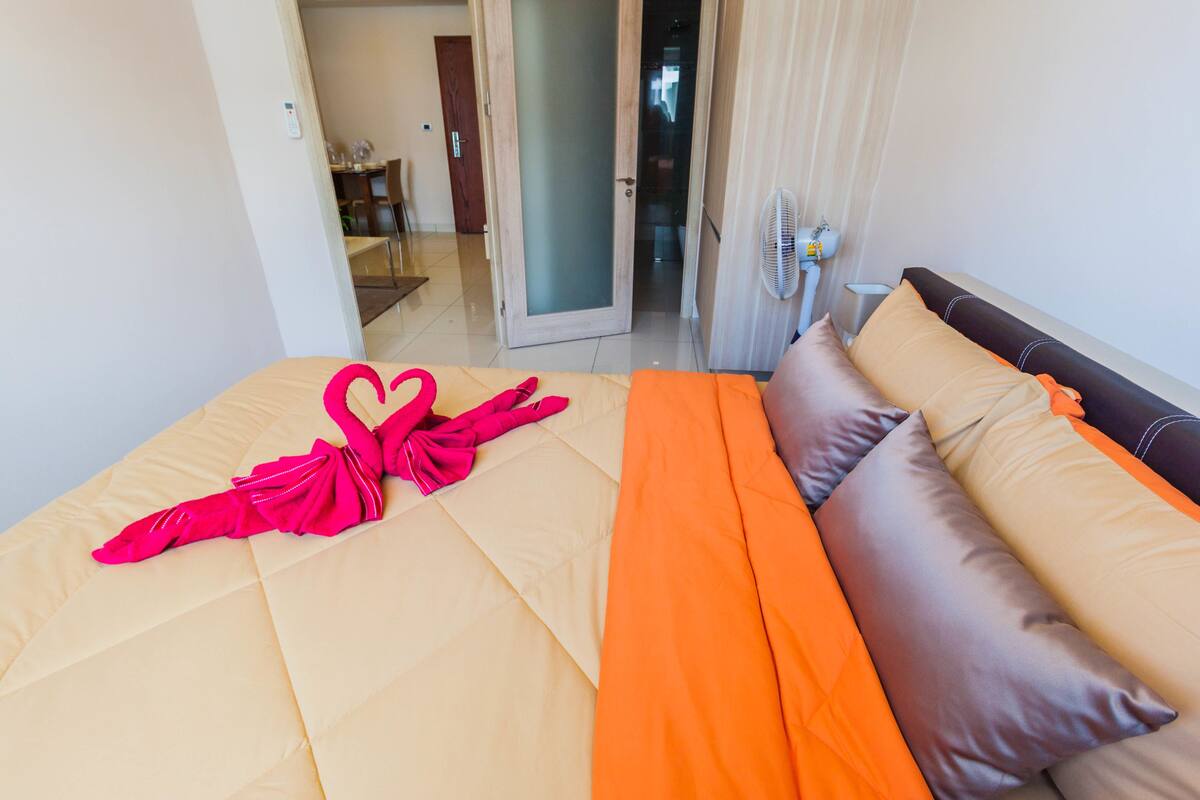 A hotel room with a bed, a fan, and a view of the dining area.