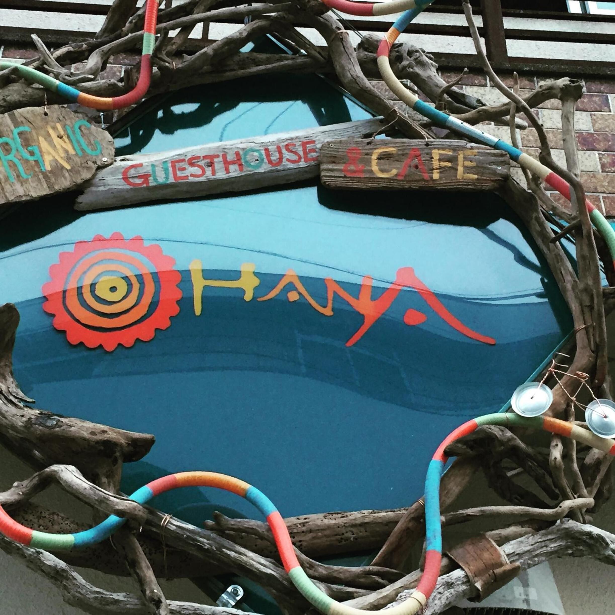 A blue car with a wooden frame decorated with colorful ropes and branches, and signs reading "GUESTHOUSE" and "CAFE".