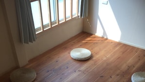 Une pièce avec un plancher en bois, deux tapis tissés, une fenêtre avec des rideaux et un interrupteur sur le mur.