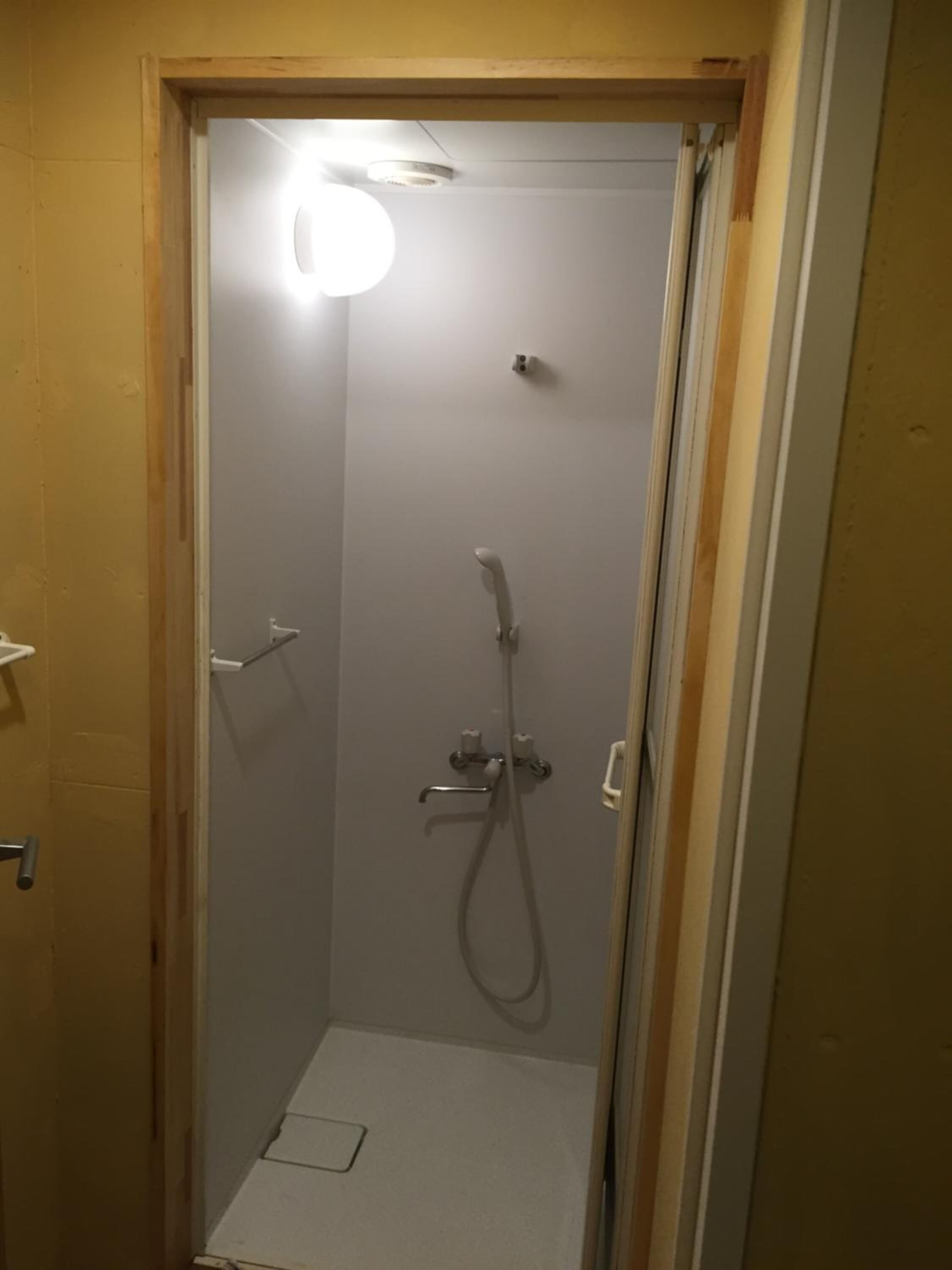 A small, enclosed shower area with a handheld showerhead and a handheld faucet.