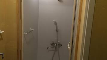 A small, enclosed shower area with a handheld showerhead and a handheld faucet.