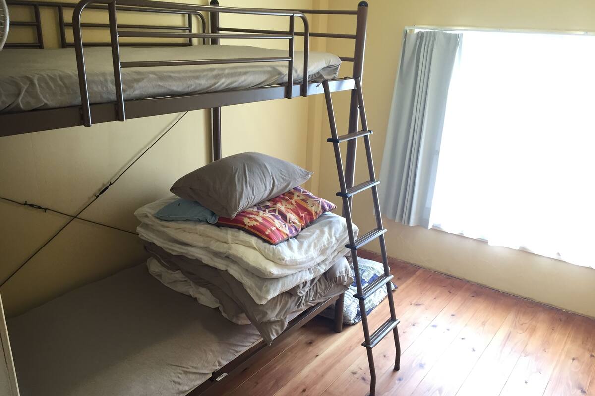 Une chambre avec un lit superposé, une échelle en bois, une fenêtre avec des rideaux et un plancher en bois.