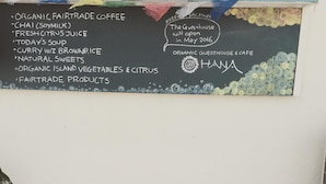 Un banc en bois avec un tableau noir servant de menu, où sont indiqués le café biologique issu du commerce équitable, le thé chai, le jus d’agrumes frais et d’autres produits.