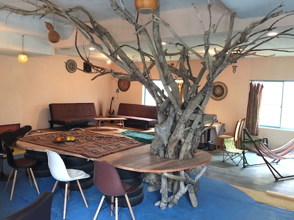 A dining area with a large wooden table surrounded by chairs, a rustic tree sculpture centerpiece, and a sofa in the background.