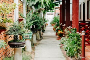 A narrow pathway lined with potted plants and a brick wall on one side. - Ngoc Qui Bungalow (Phu Quoc)