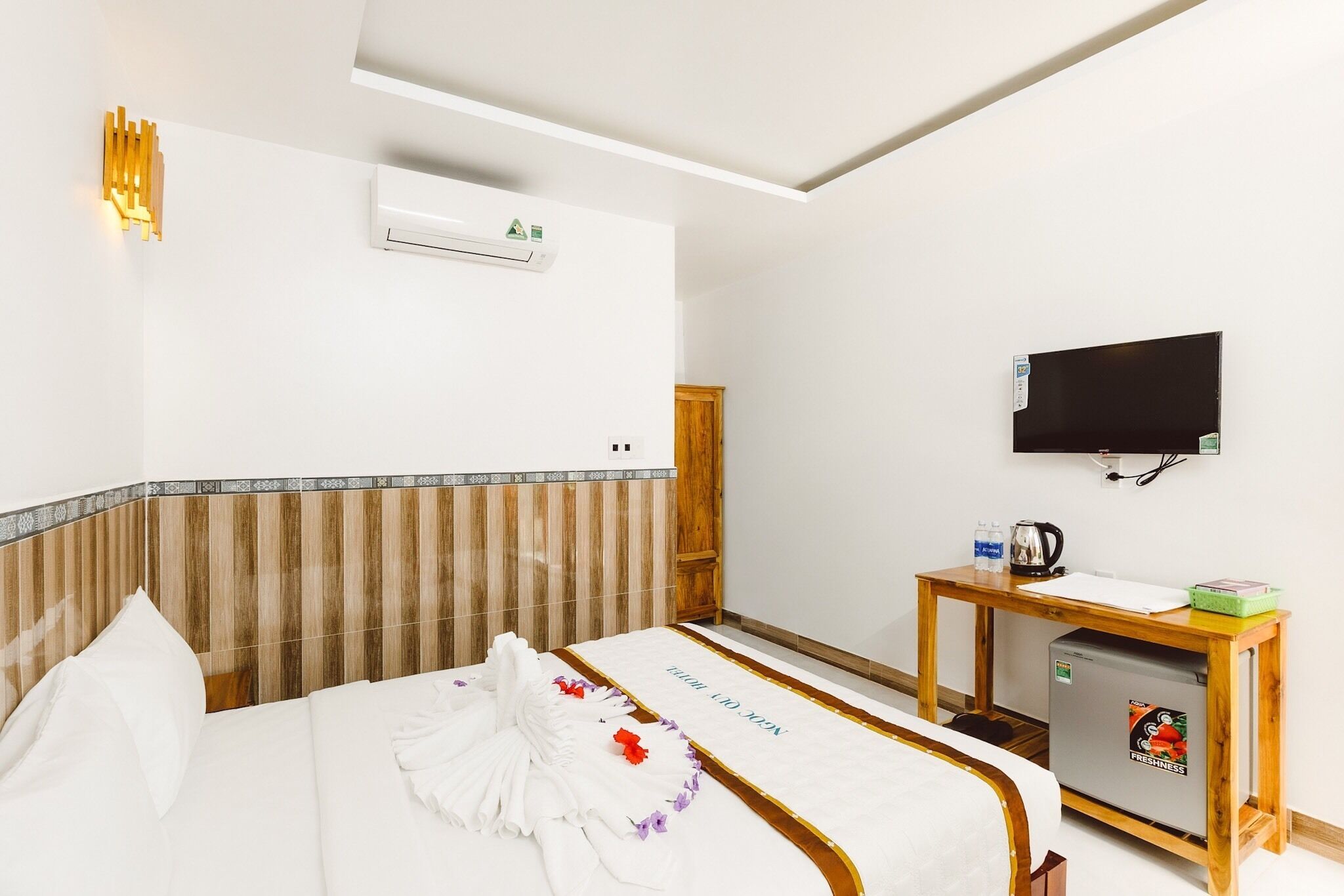 Une chambre d’hôtel avec un lit, une table de chevet en bois, une télévision et un réfrigérateur.