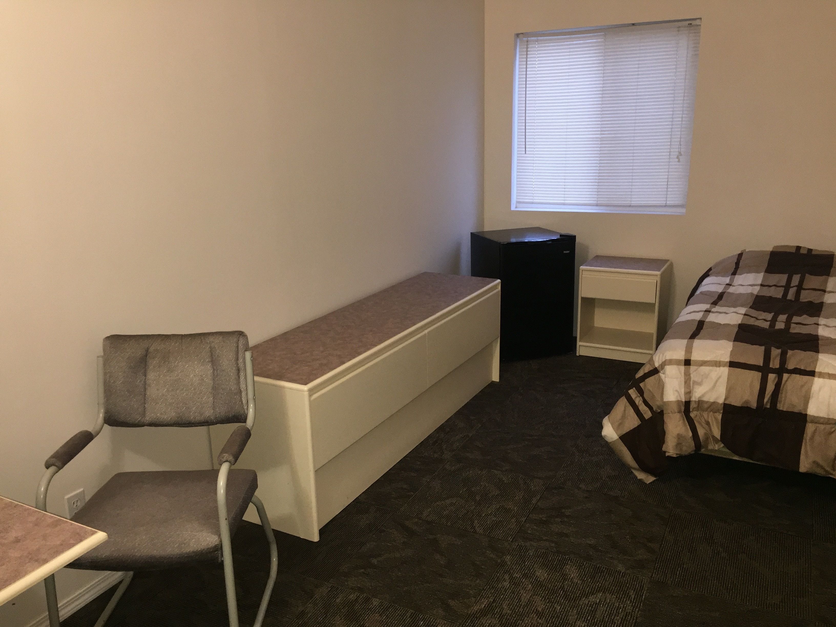 Een kleine, compacte kamer met een bureau, stoel en een bed met een geruit plaid.