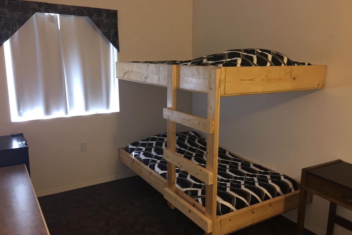 Uma cama beliche com colchão estampado, uma mesinha e uma janela com cortinas.