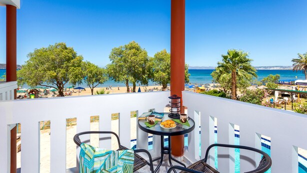 Un balcón con una mesa para dos, con vista a una playa con palmeras y el mar.