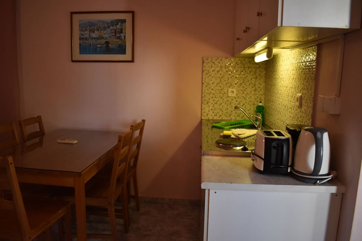 Une petite cuisine avec une table à manger, des chaises, un grille-pain, une bouilloire et un égouttoir vert.