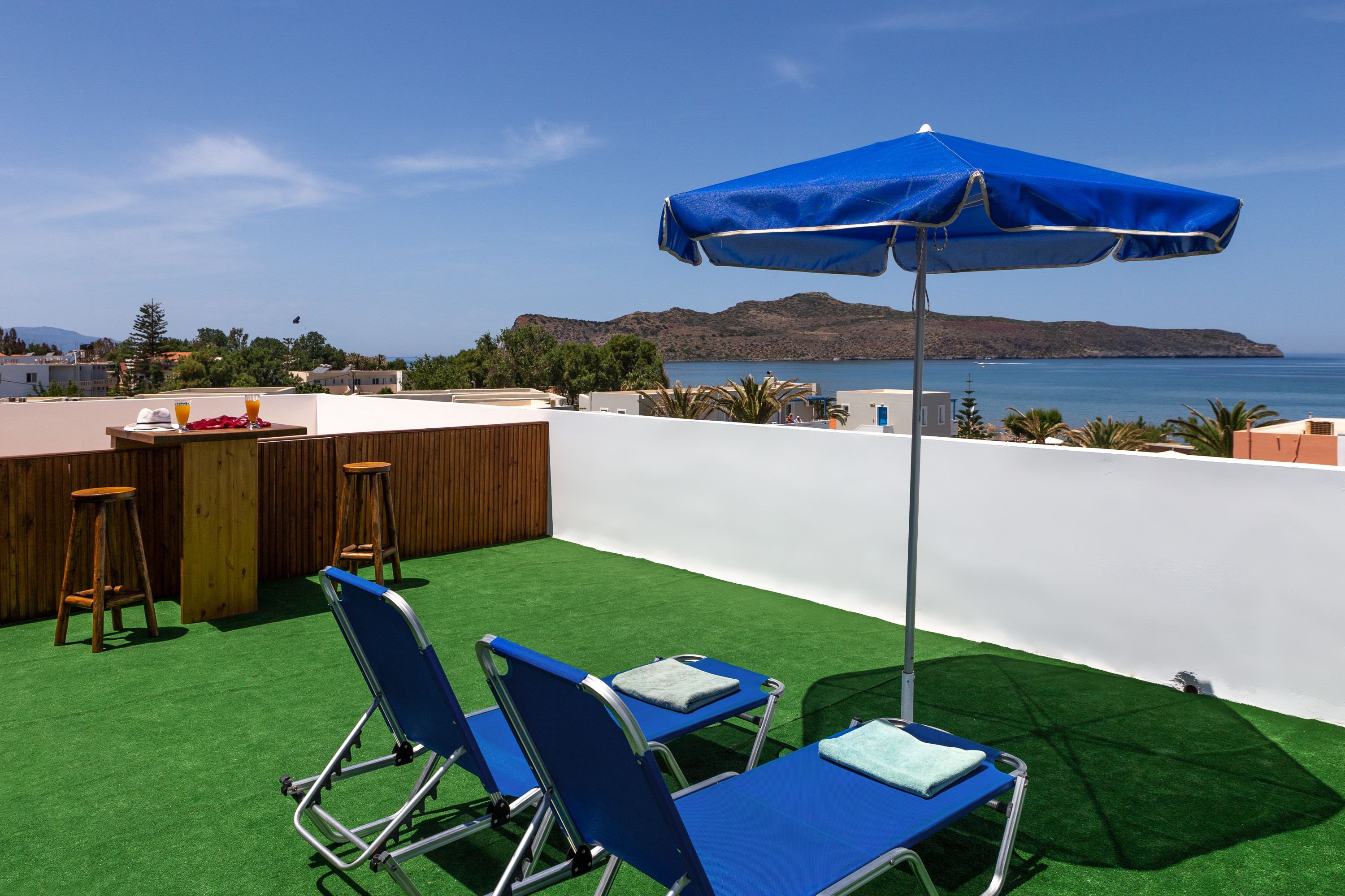 An outdoor seating area with two blue lounge chairs, a bar with stools, and a blue umbrella.