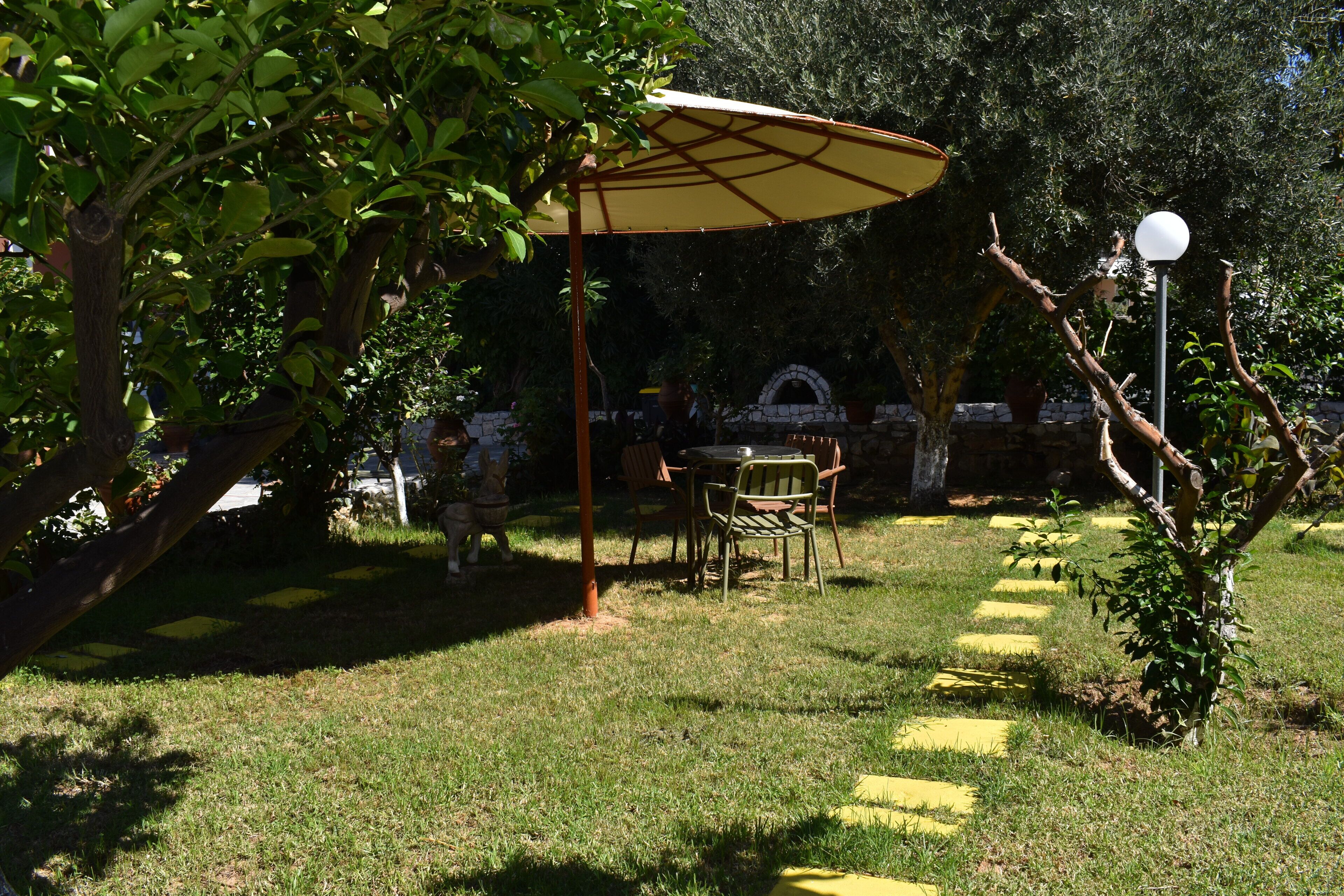 Un'area patio con tavolo e sedie riparata da un tetto, circondata da vegetazione e un muro in pietra.