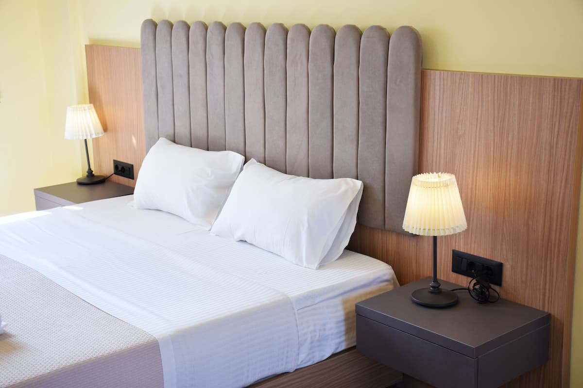 Un lit bien fait, avec du linge de lit blanc, deux tables de chevet avec des lampes et une tête de lit en bois.