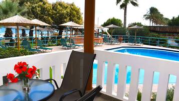 Área de piscina com espreguiçadeiras, uma mesa com um vaso de flores e vista para a piscina e o oceano.