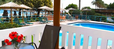 A poolside area with lounge chairs, a table with a vase of flowers, and a view of the pool and ocean.
