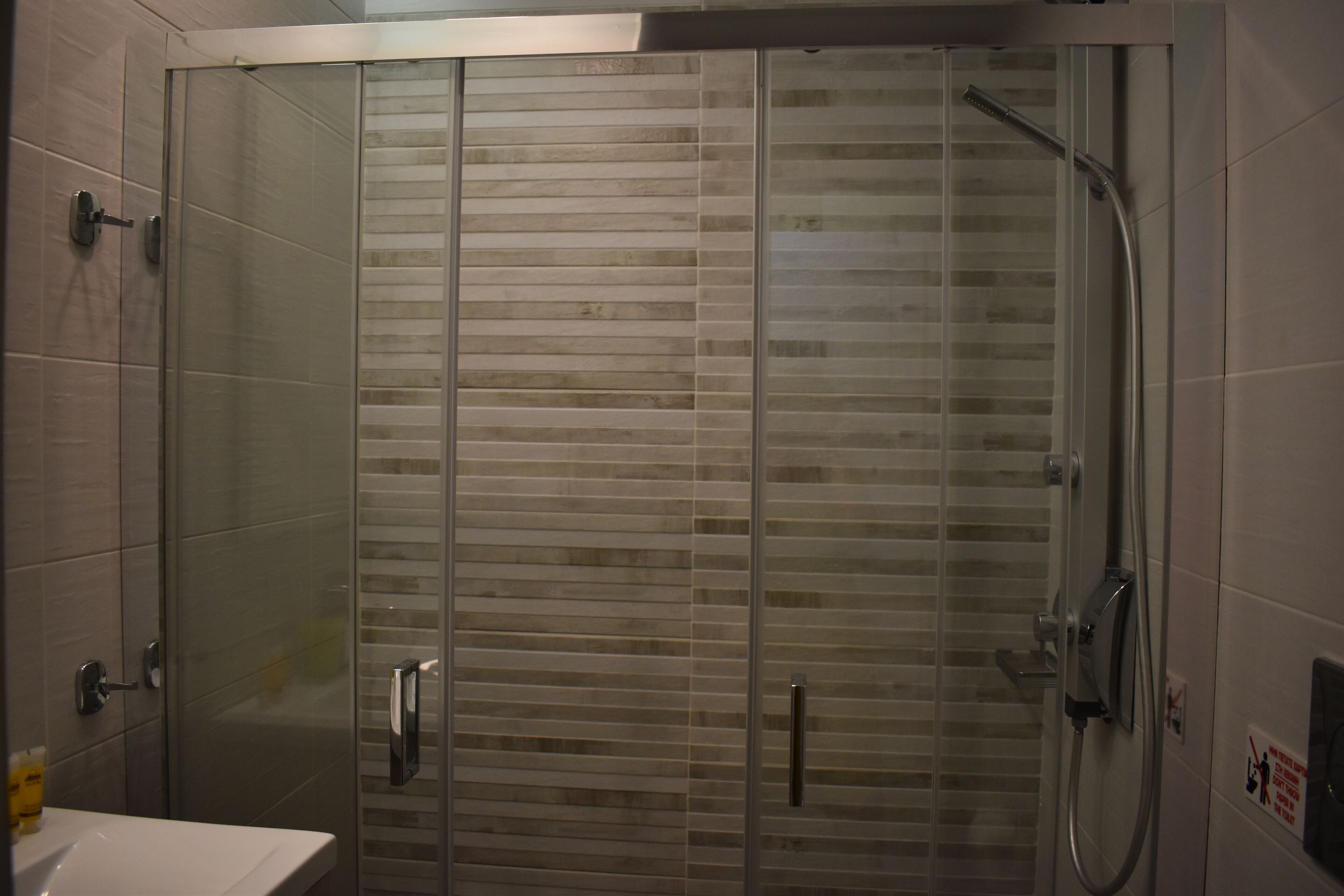 Une salle de bain moderne avec une douche à l’italienne en verre, un lavabo blanc et un mur recouvert de carreaux.