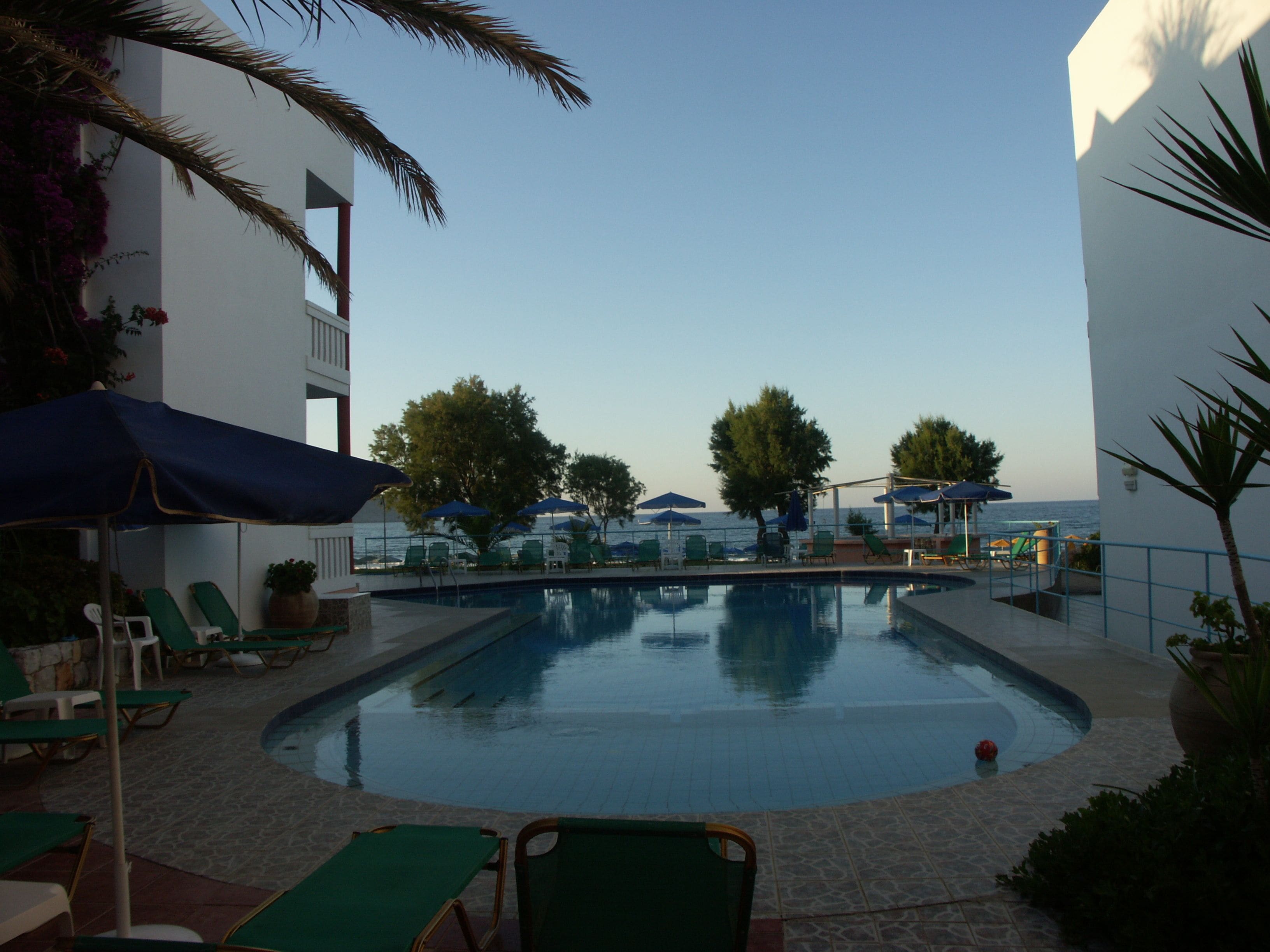 A pool area with lounge chairs and umbrellas, surrounded by buildings and trees.