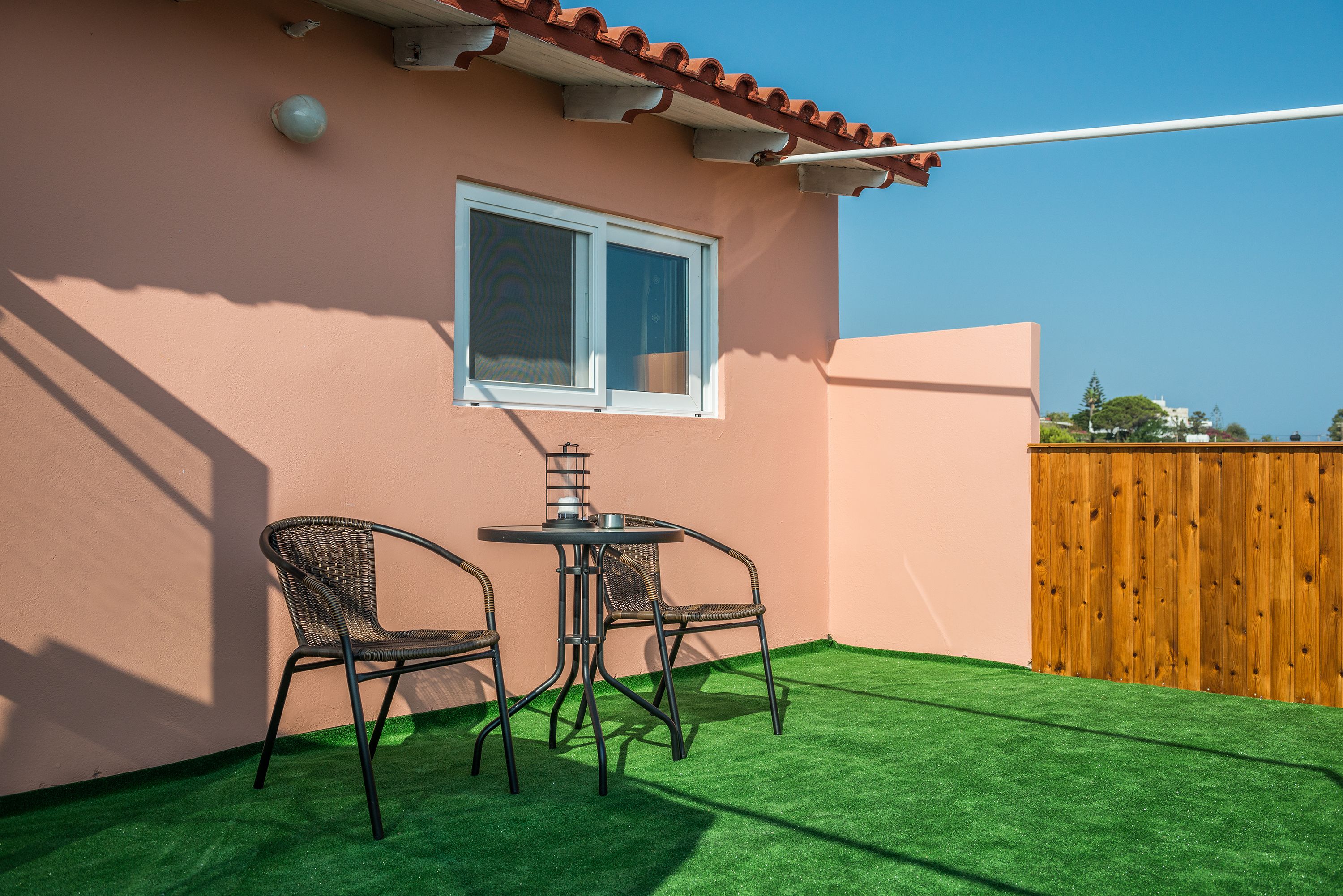 Une terrasse avec un revêtement de gazon synthétique, une clôture en bois et deux fauteuils en osier disposés autour d’une table.