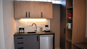 Una cocina compacta con armarios de madera, lavavajillas, cafetera y hervidor.