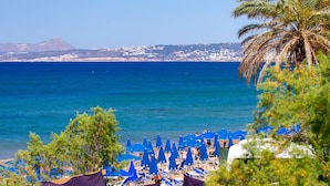Una playa con sombrillas azules y una montaña al fondo.