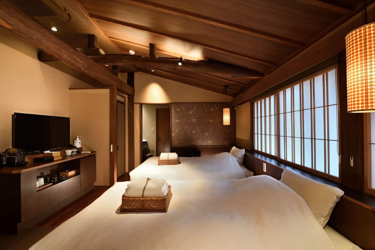 A hotel room with two beds, a TV, a wooden ceiling, and large windows.
