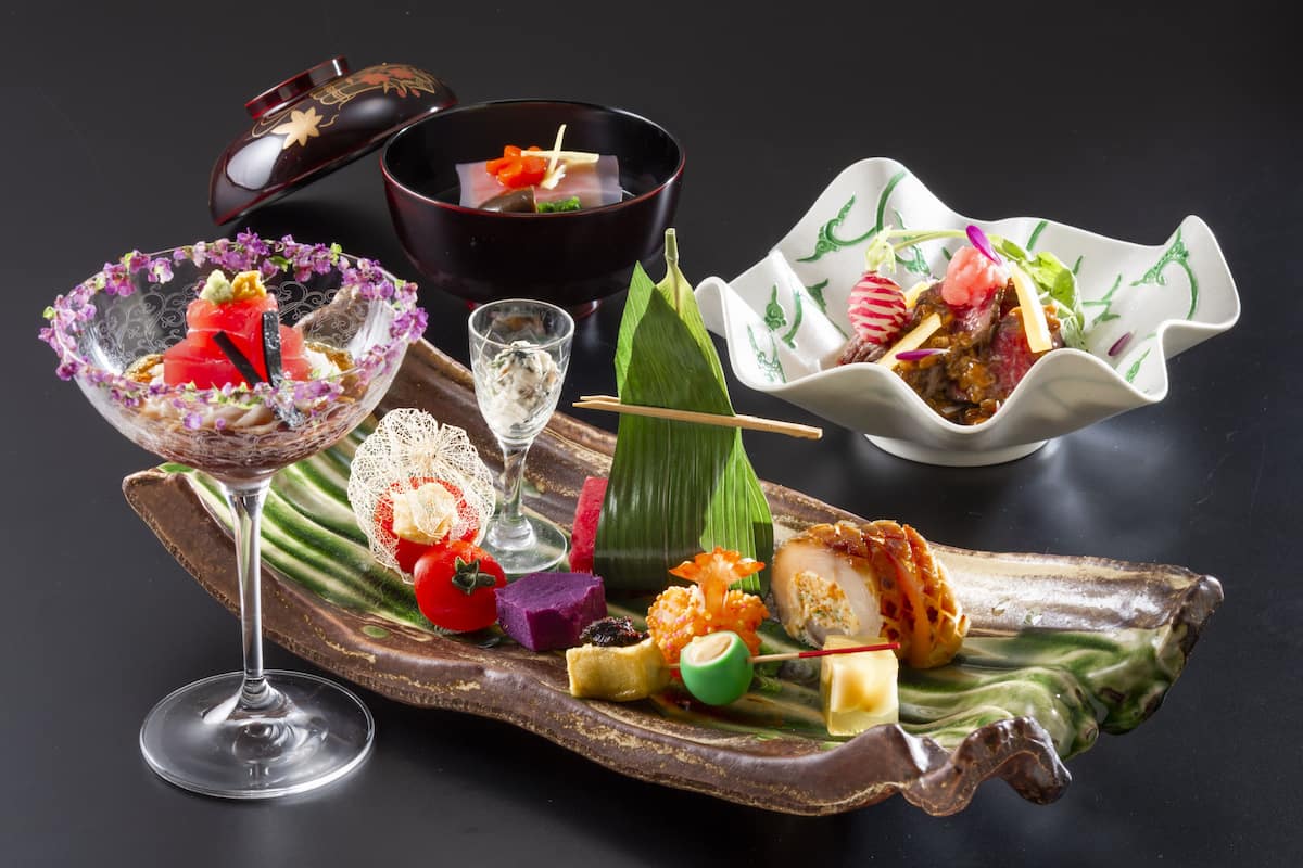 A variety of Japanese dishes on a wooden serving board, including sushi, sashimi, and a glass of sake.
