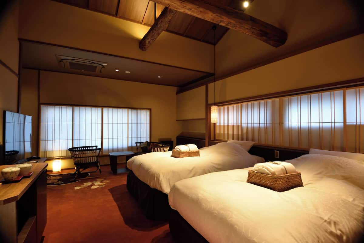 A hotel room with two beds, a desk, a chair, and a window with blinds.