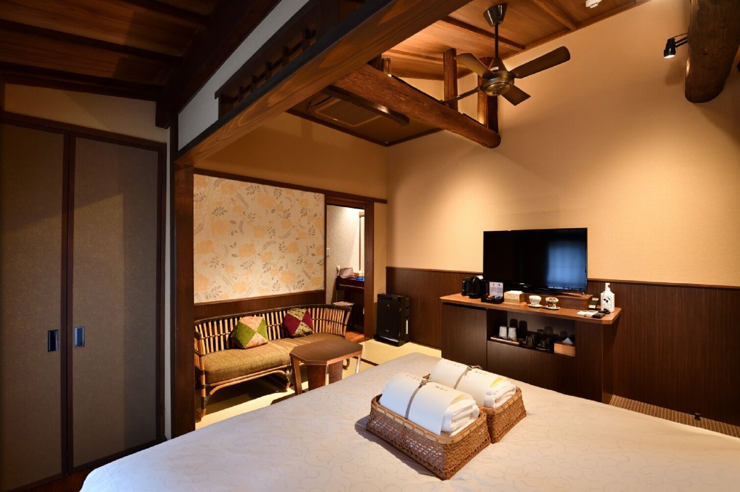 A hotel room with a bed, a television, a sofa, a ceiling fan, and a wooden cabinet with a TV stand.
