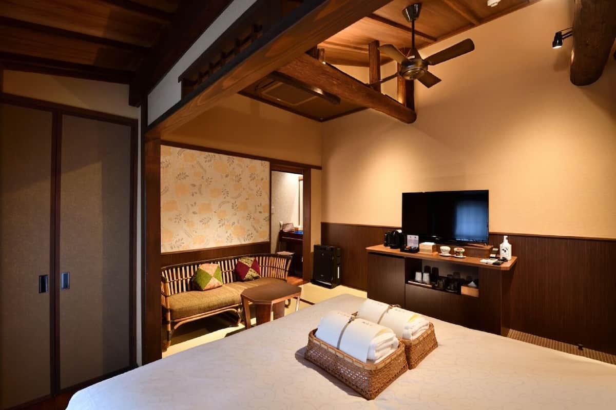 A hotel room with a bed, a television, a sofa, a ceiling fan, and a wooden cabinet with a TV stand.