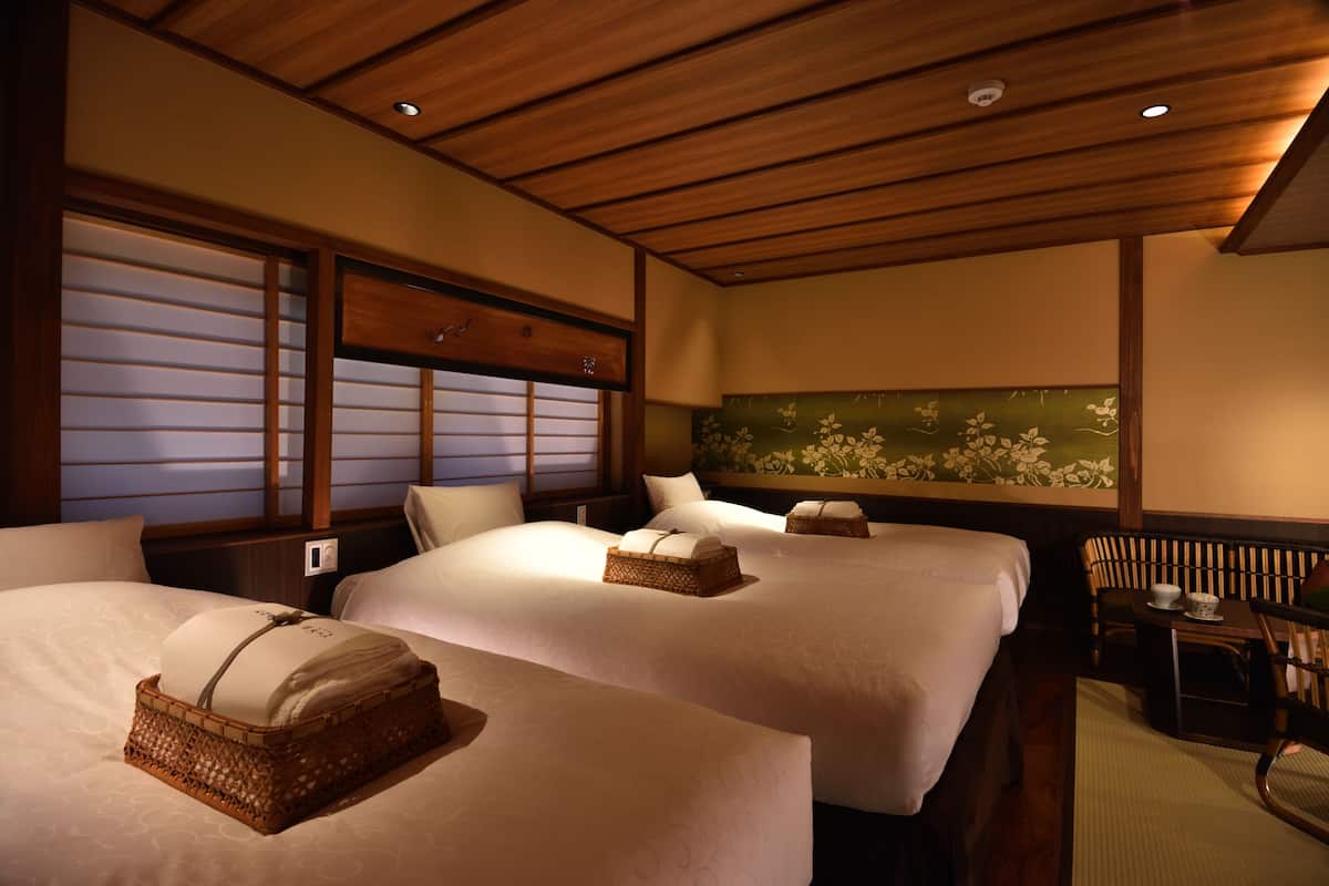 A hotel room with two beds, wooden ceiling, and a green floral wall.