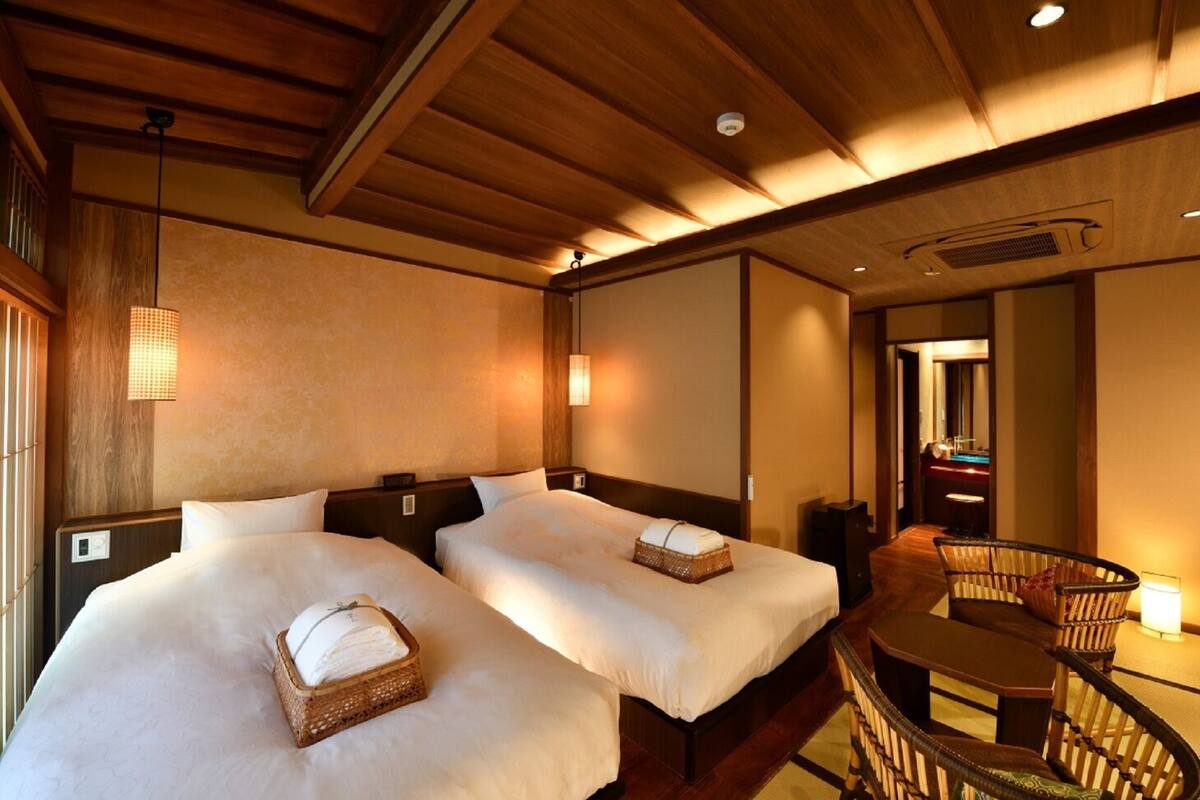 A hotel room with two beds, a small table, a chair, and a mirror.