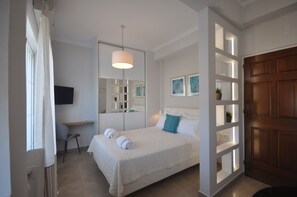 A bedroom with a bed, a desk, a chair, a TV, and a door with a wooden panel. - Chania Apartments (Chania)