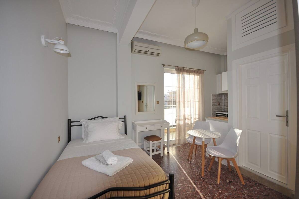 A bedroom with a bed, a desk, a chair, a mirror, and a door.