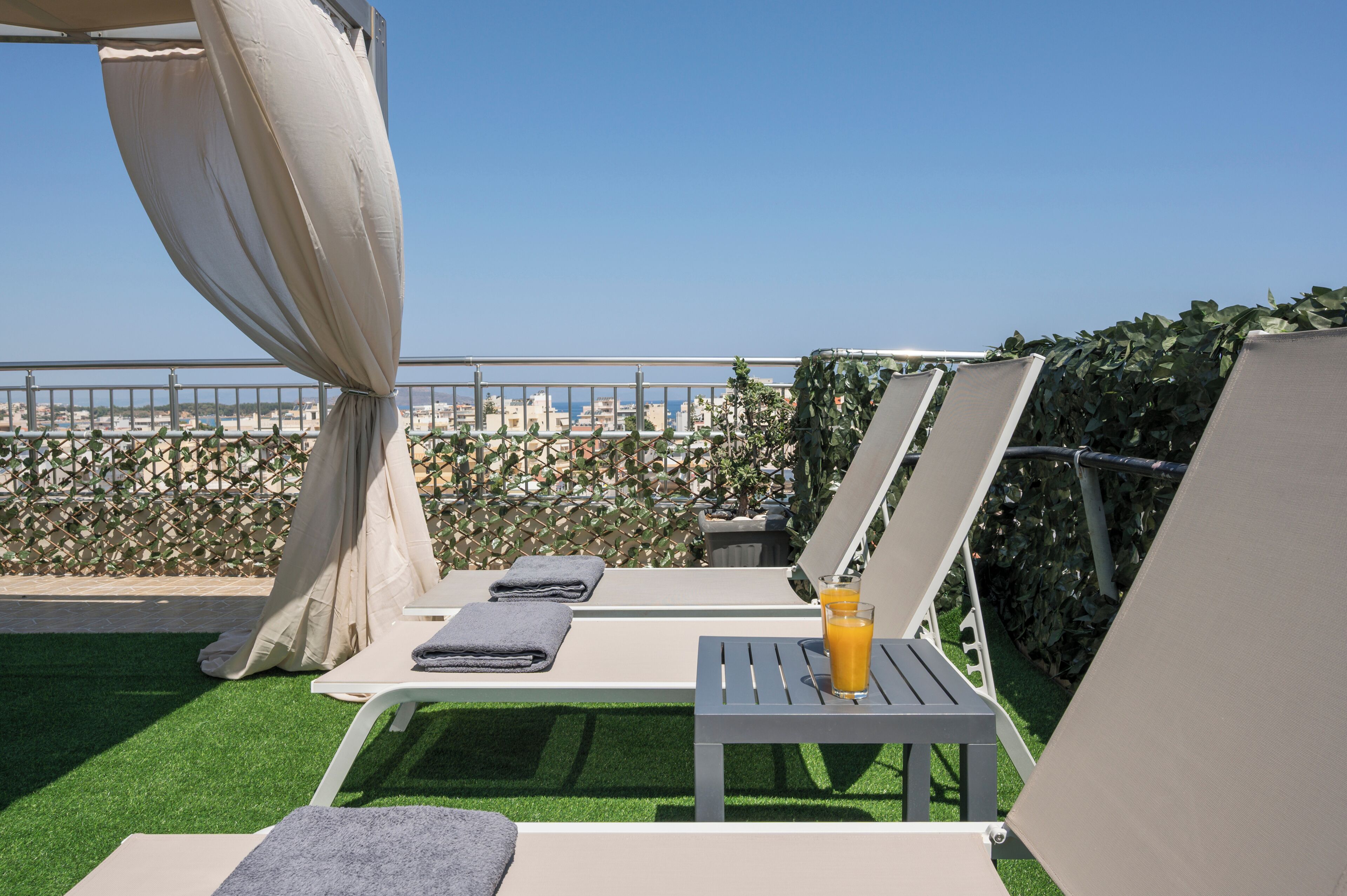 Eine Dachterrasse mit Liegestühlen, einem Tisch mit einem Getränk und Blick auf die Skyline.