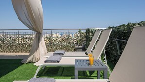 Eine Dachterrasse mit Liegestühlen, einem Tisch mit einem Getränk und Blick auf die Skyline.