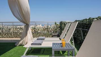 Eine Dachterrasse mit Liegestühlen, einem Tisch mit einem Getränk und Blick auf die Skyline.
