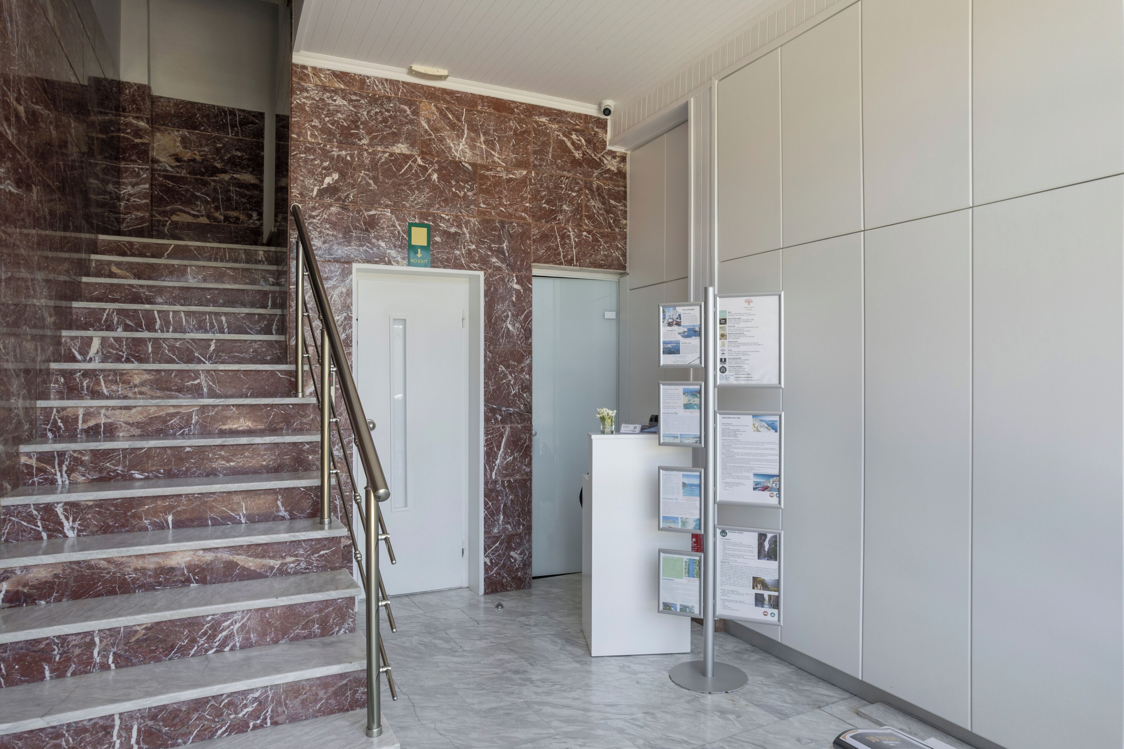 Eine Marmortreppe, ein Empfangstresen mit Informationsschildern und eine Tür.