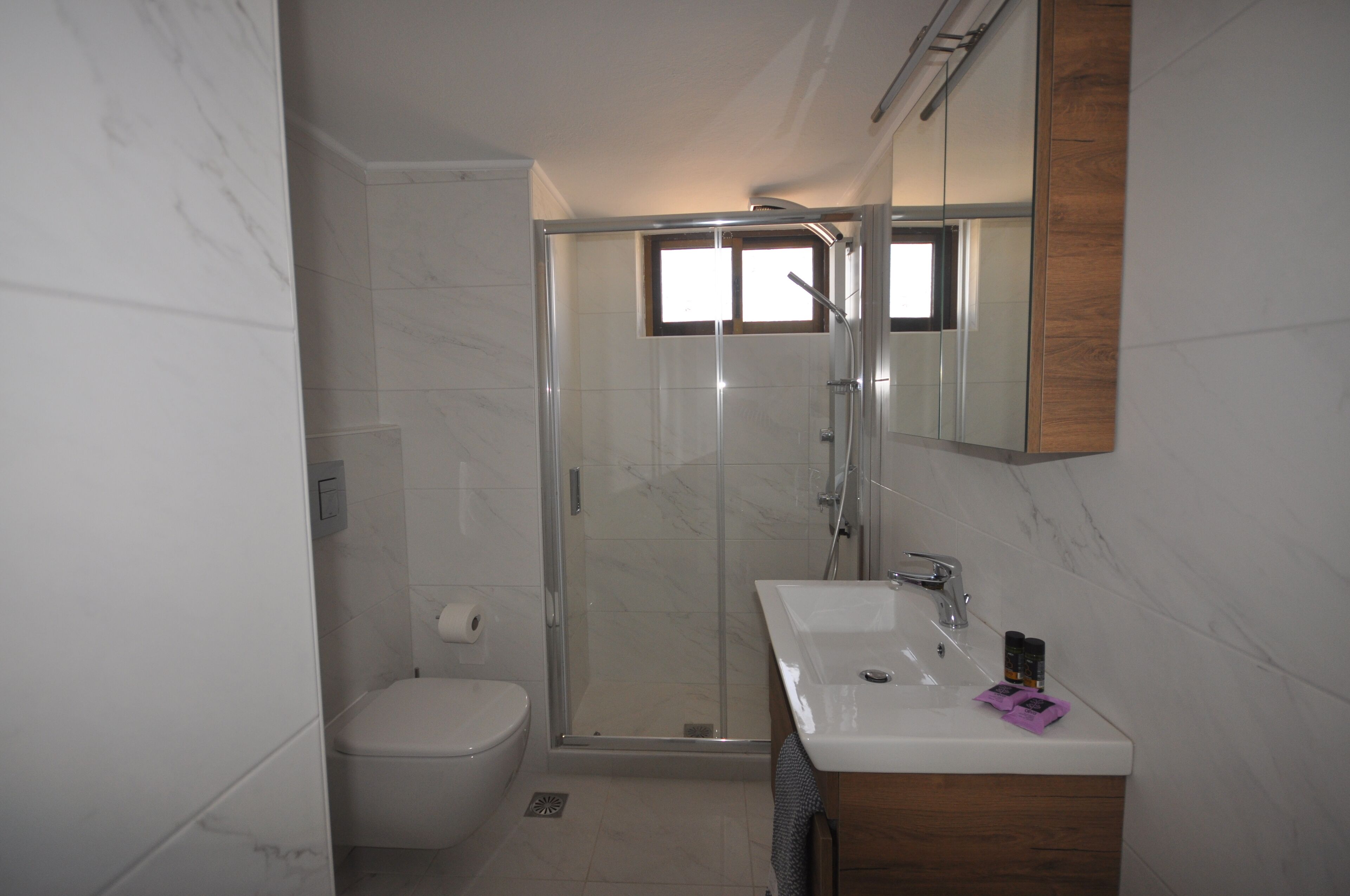 A modern bathroom with a glass-enclosed shower, a white sink, and a wooden vanity.
