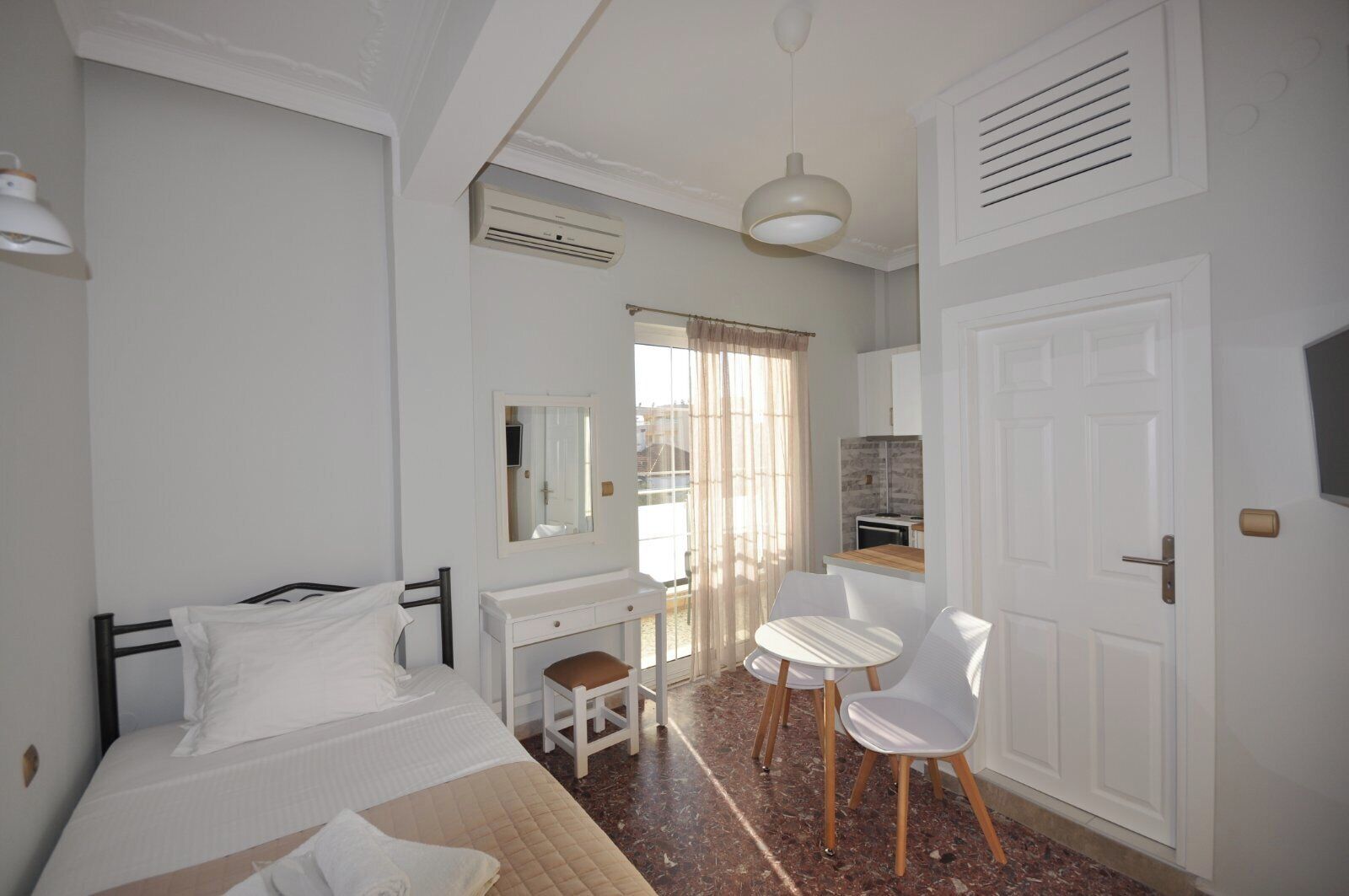 A bedroom with a bed, a desk, a chair, a mirror, and a door.