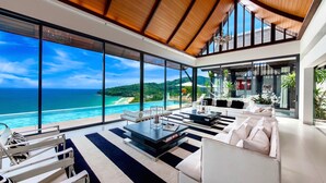 Un salon moderne doté d’une grande baie vitrée donnant sur une plage et l’océan.