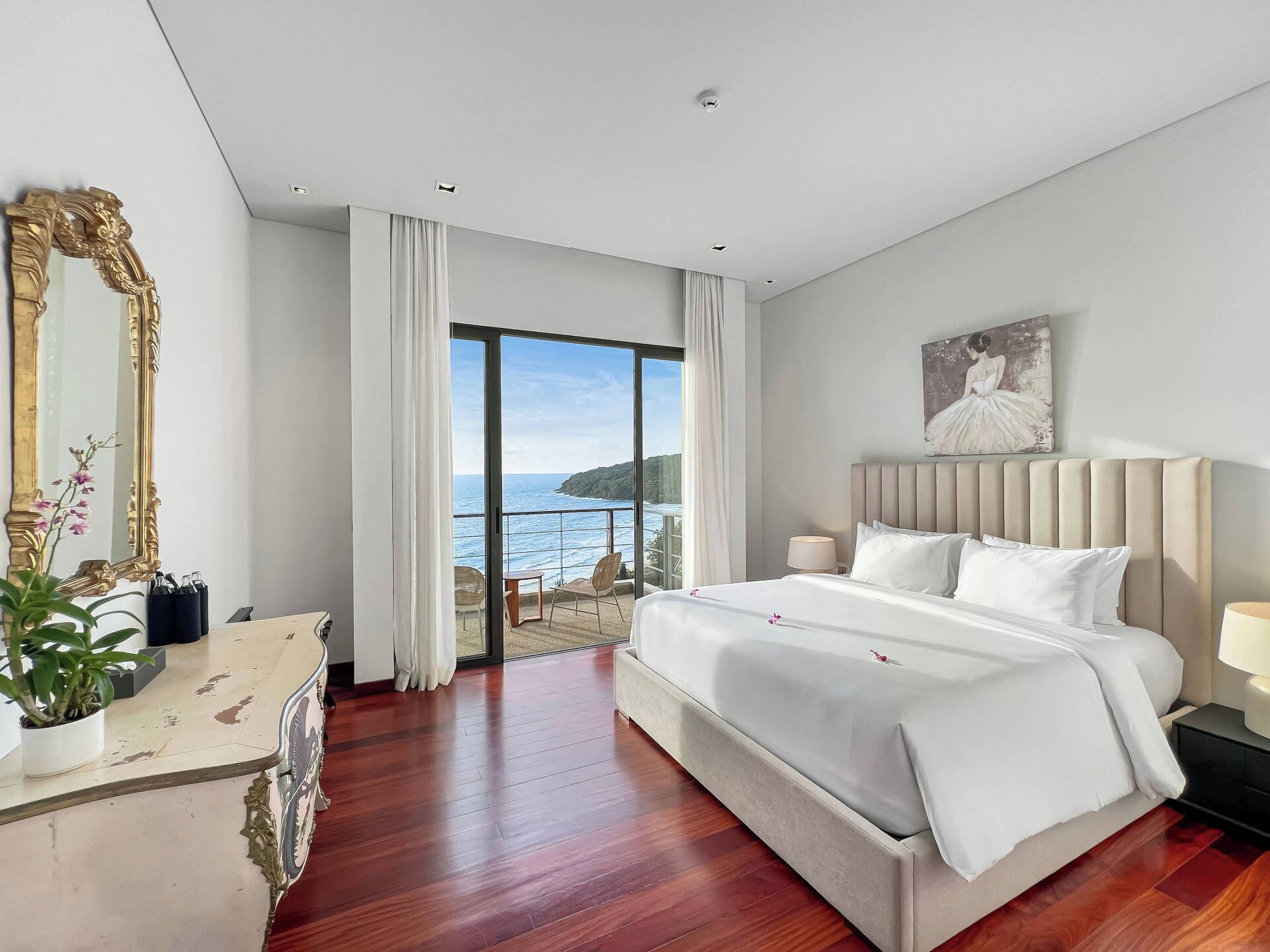 Une chambre avec un grand lit, un miroir, une commode et une vue sur la mer.